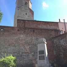 Mury Obronne z widocznymi zamurowanymi okrągłymi oknami dawnych zabudowań zamkowych, w tle wieża zamkowa, na pierwszym planie pomnik 700- i 750-lecia Bierutow